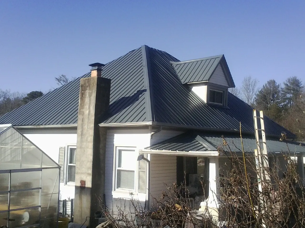 Dark blue standing seam metal roof on a white farmhouse with dormer — Slate & Tile Roof Repair by Roofing Brothers in Corrales