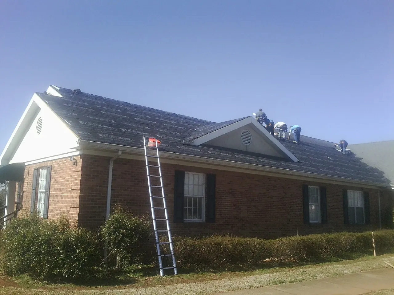 Crew tearing shingles off a brick ranch roof with a ladder set — Emergency Roof Repair work by our crew in Corrales