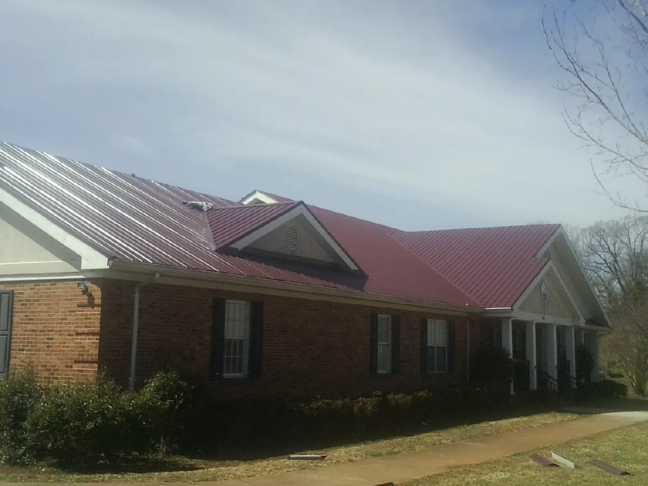 Red metal roof with gabled entries on a long brick building, from a Hail Damage Roof Repair job in Corrales
