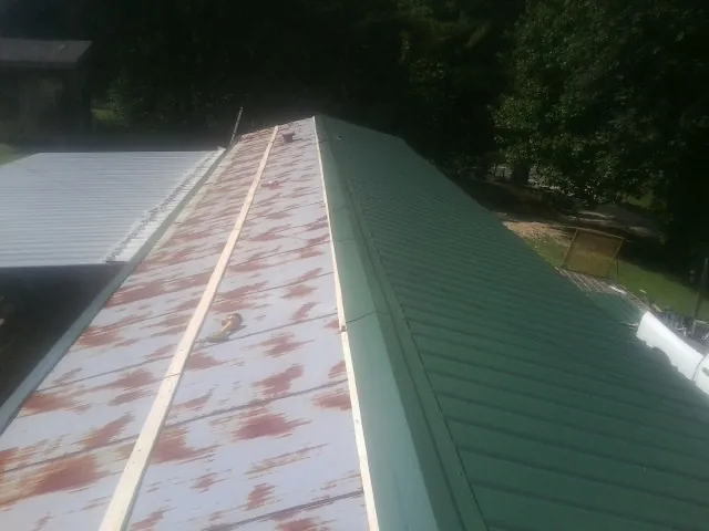 Old rusted panels beside newly installed green metal roofing — Wind Damage Roof Repair by Roofing Brothers in Corrales
