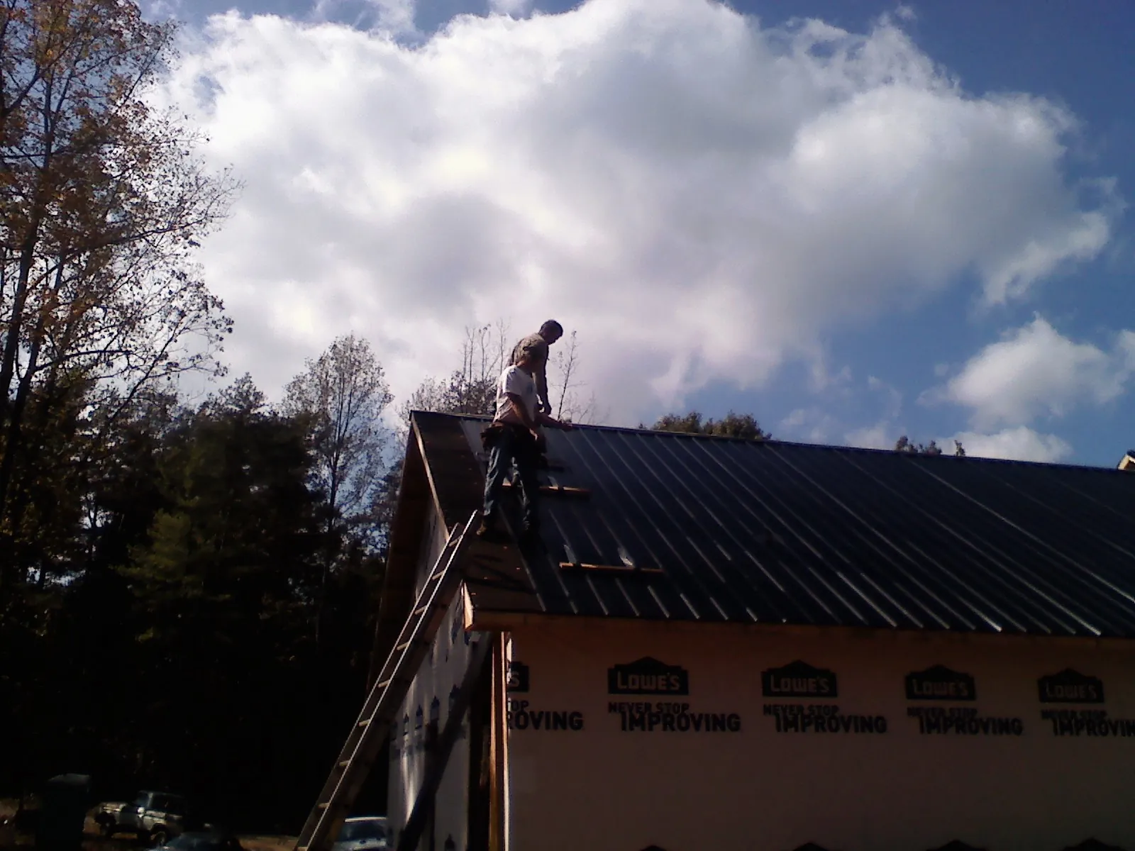 Roofer fastening dark metal panels high against a cloudy sky, from a Roof Inspection job in Corrales