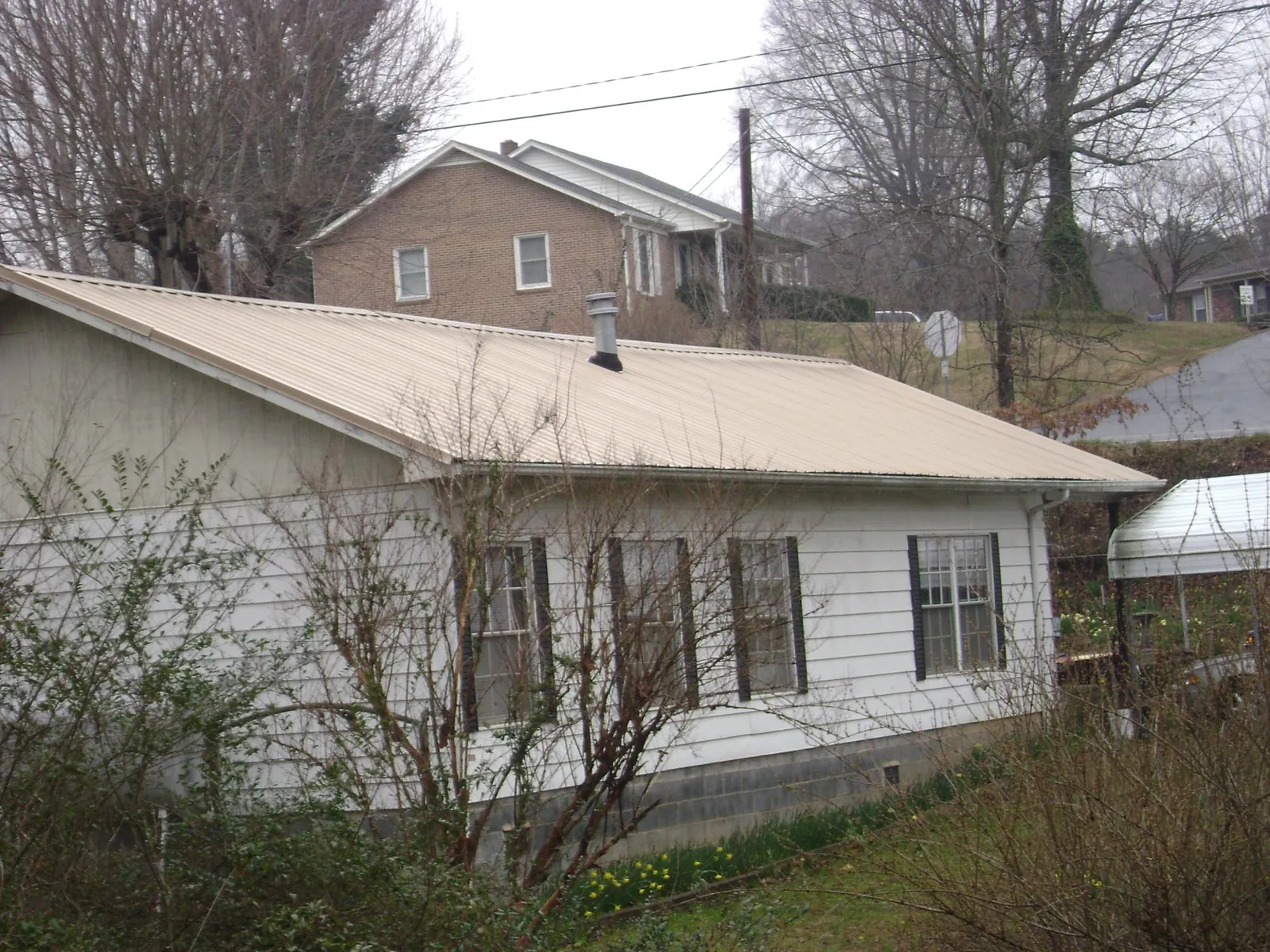 Tan metal roof on a white sided house set into a hillside — Commercial Roofing by Roofing Brothers in Corrales