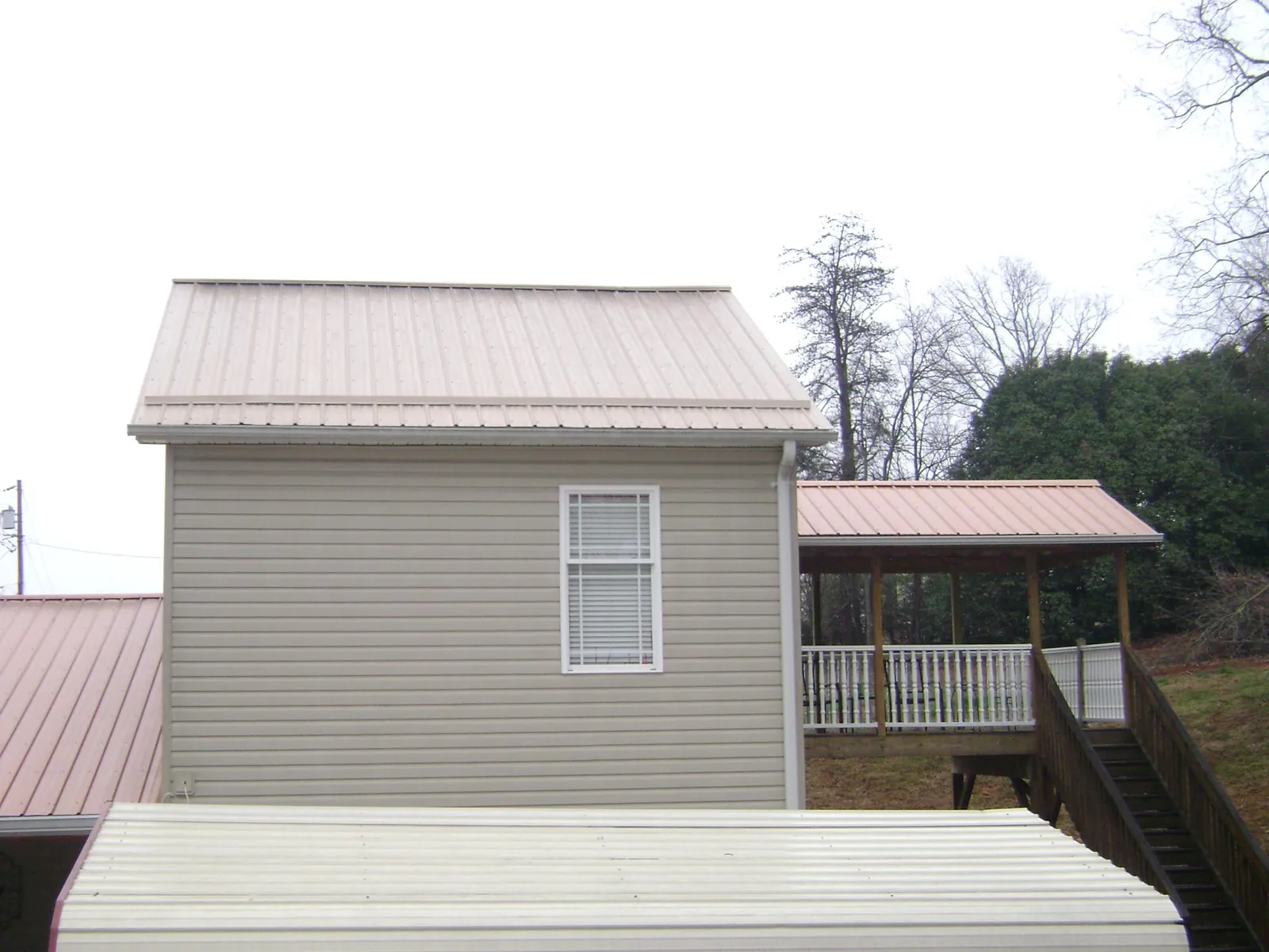 Tan metal roofs on a two story addition and attached porch, from a Roof Replacement job in Corrales